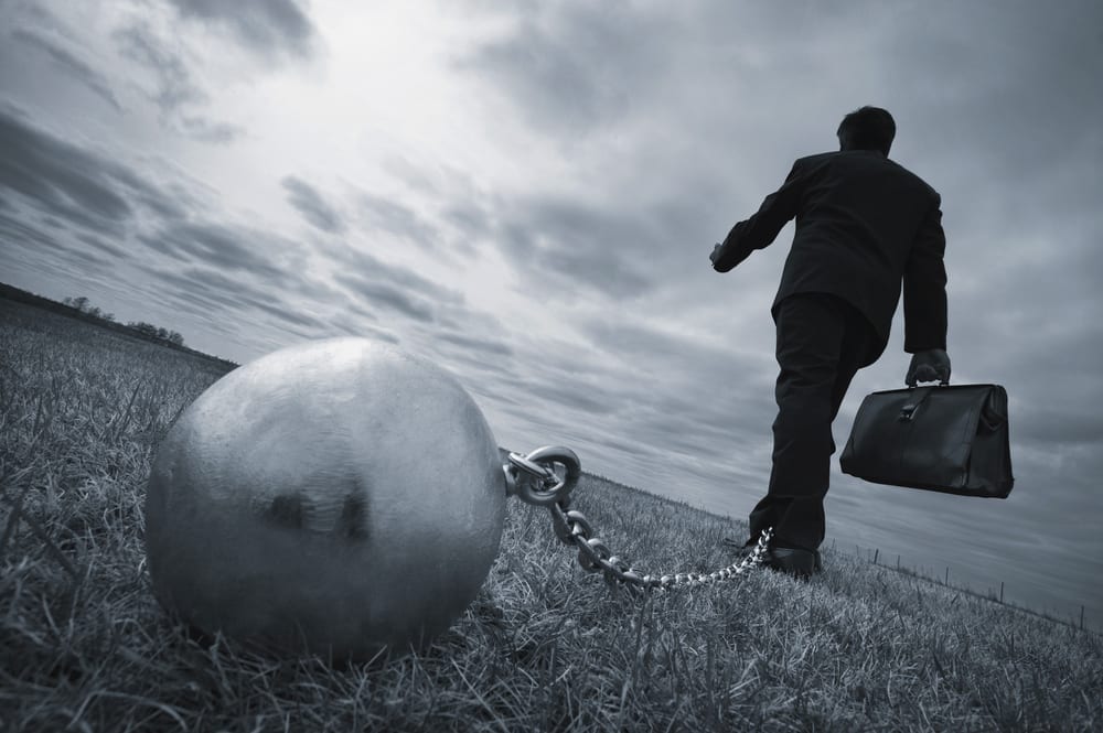 A business person shackled with a ball and chain