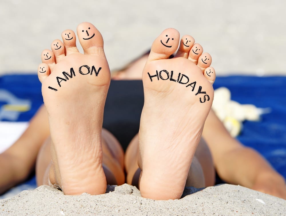 A pair of bare feet with "I am on holidays" written on the bottom
