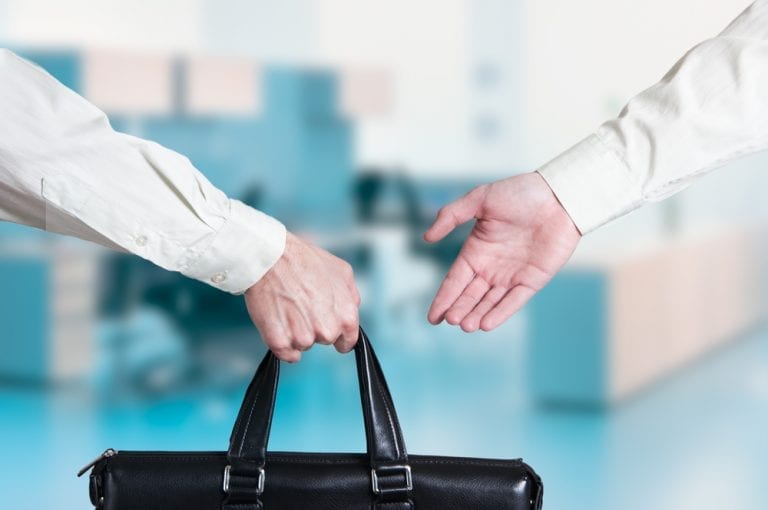 Two business people, one is handing a briefcase to the other