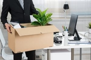 A person holding a box of personal items stood next to their desk
