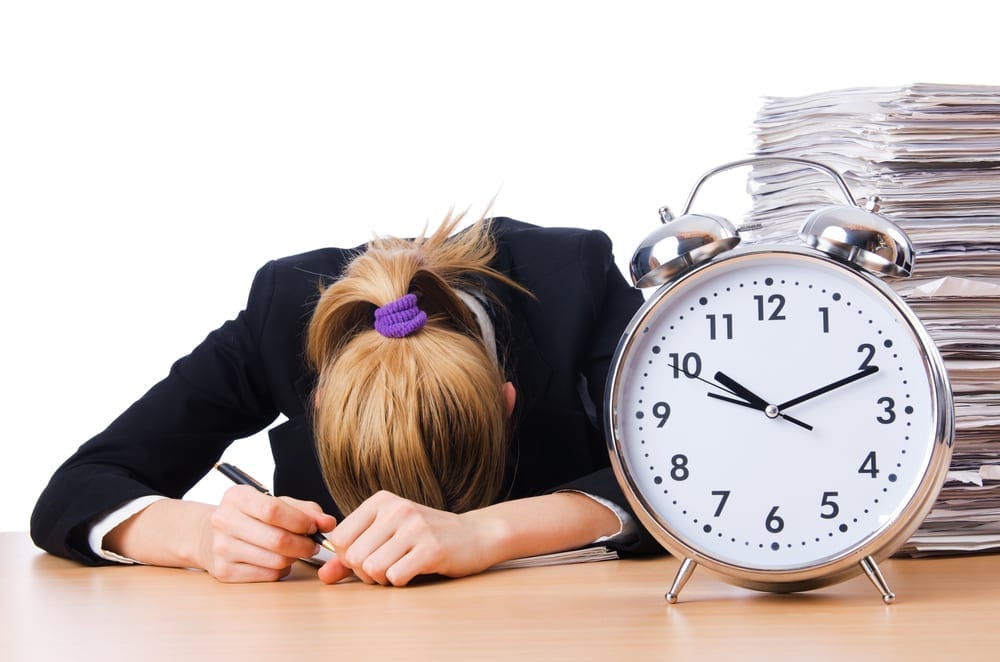 Large clock on a desk with a female head bowed resting on the table