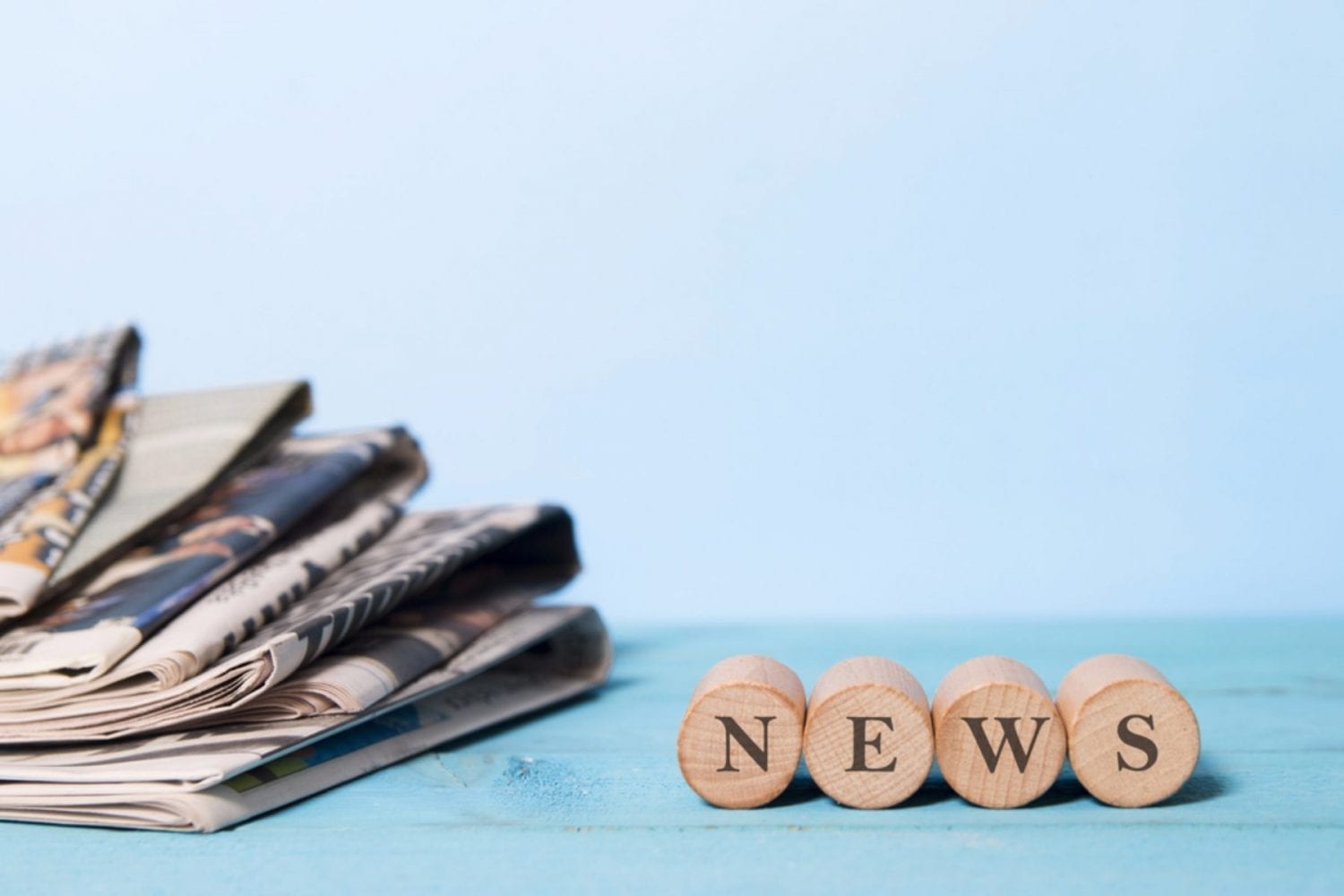 Pile of Newspapers on the left hand side of a table with the word news on the right hand side spelt out on circular printing stamps