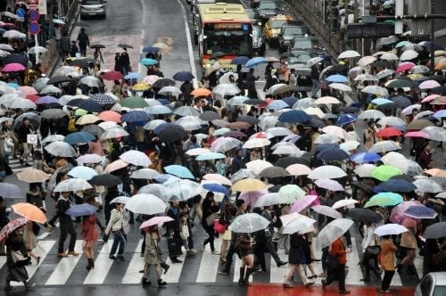 A busy street crossing with lots of people using colourful umbrellas