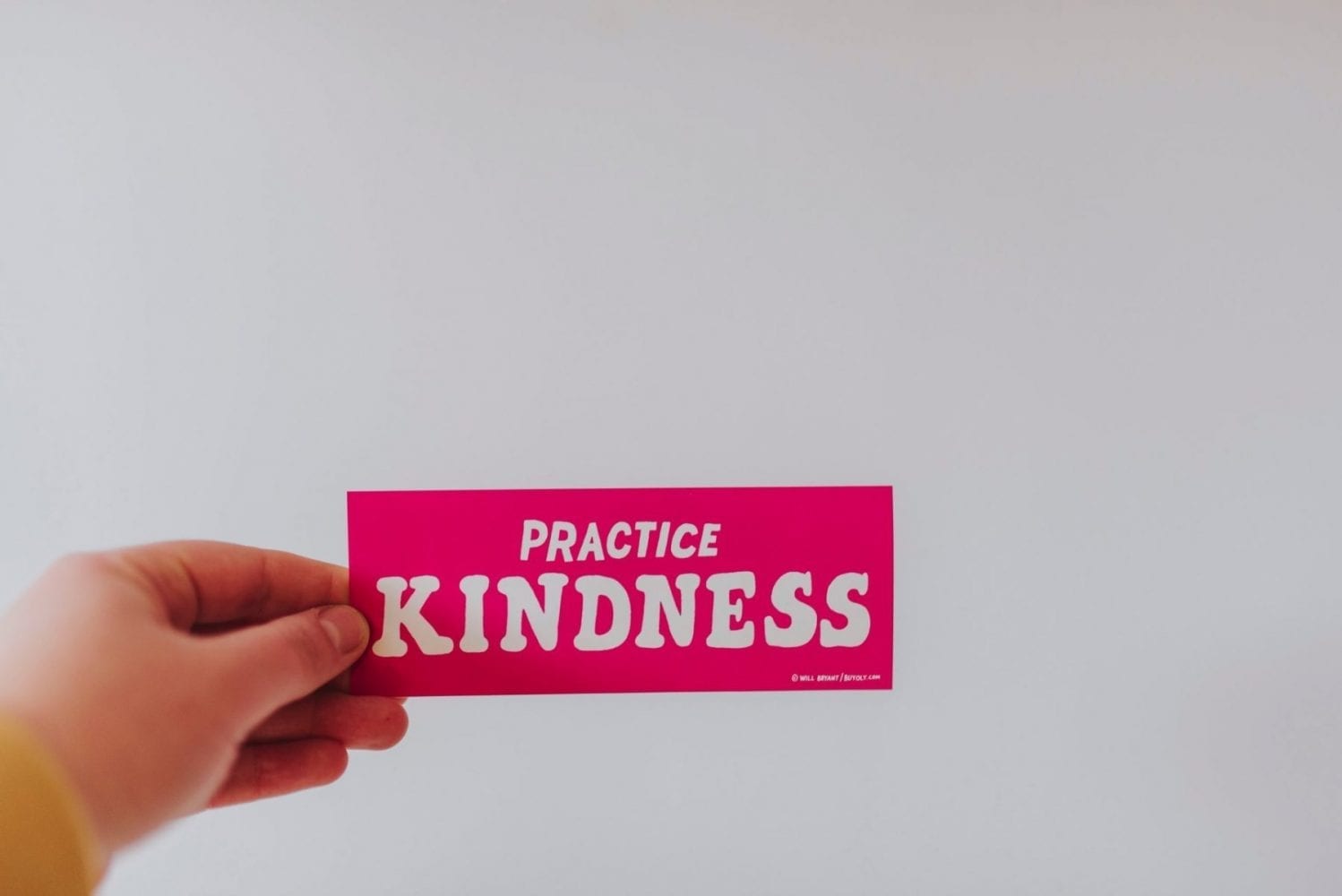 Hand holding a tab of paper with the words "Practice kindness"