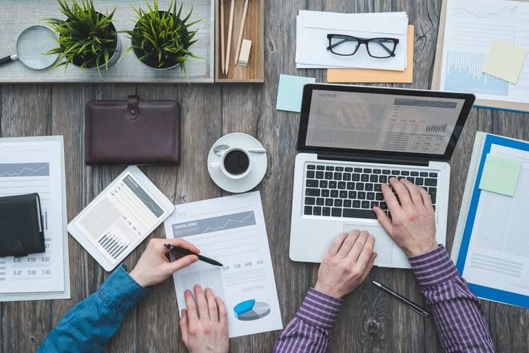 Two people at a desk with lots of documents and papers scattered around