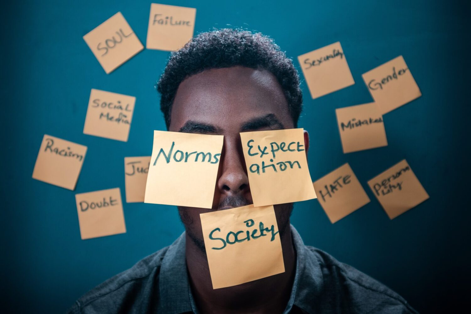 Photo of a person with sticky notes attached to their face with the words "Norms", "Expectation" and "Society"