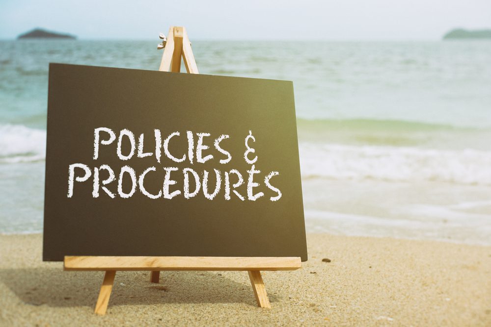 A blackboard sign on a beach that reads "Policies & Procedures"