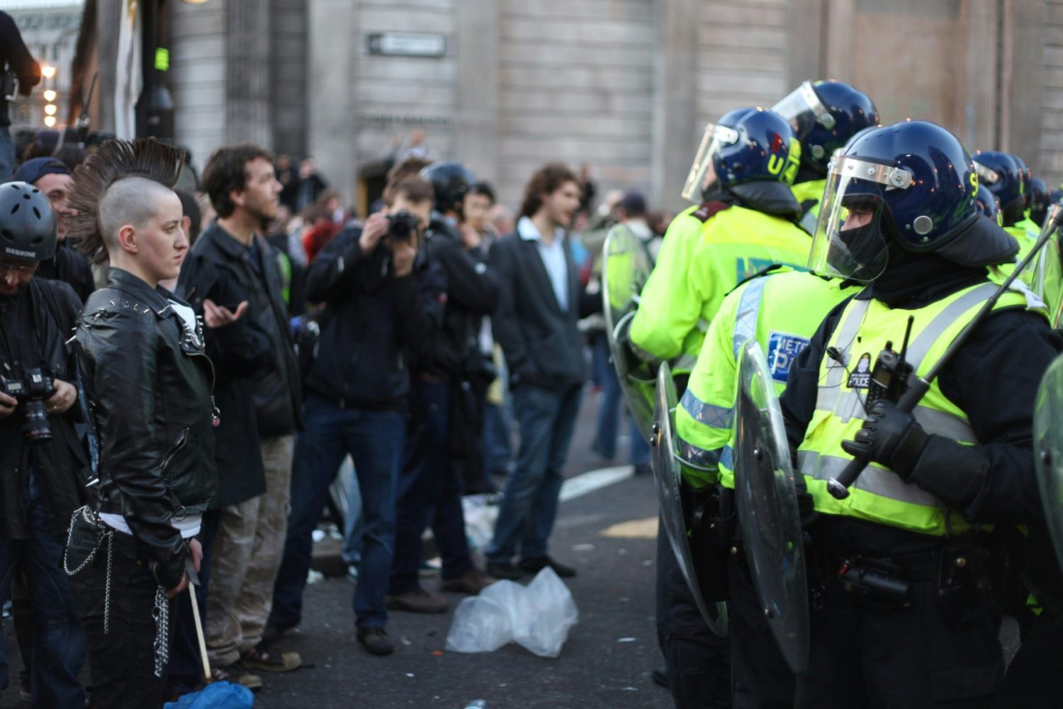 line of policeman with shields holding a crowd back